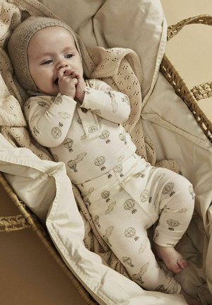 Helle Creme Baumwollpyjamas mit einem gerippten Muster, die mit einem verspielten Ballon-Print gestaltet sind. Das Baby liegt in einem geflochtenen Korb, der mit einer gestrickten Decke ausgelegt ist.