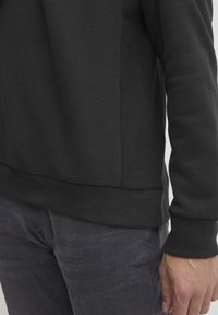 Sudadera negra con puños y dobladillo acanalados, hecha de una tela suave. Presenta un corte recto y costuras mínimas para un acabado limpio.