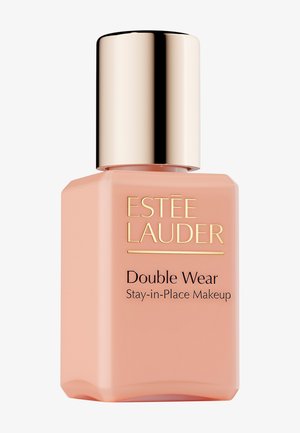 Botella cuadrada de vidrio color durazno claro con tapa metálica dorada, con texto negro que dice "Double Wear Stay-in-Place Makeup" en fuente elegante.