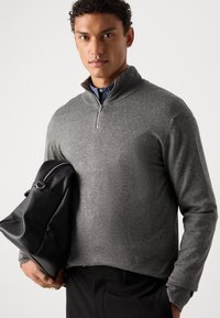 Gray zip-neck sweater made of textured fabric, paired with a black leather bag. The sweater has long sleeves and a fitted design.