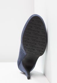 Chaussure à talon haut en daim bleu foncé avec un bout pointu, dotée d'une semelle extérieure en caoutchouc noir texturée embossée du nom de la marque.