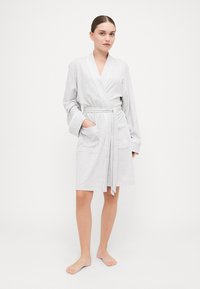 Accappatoio in cotone grigio chiaro con cintura, maniche ampie, due tasche frontali e un dettagliato logo discreto sulla tasca. Tessuto morbido e testurizzato.
