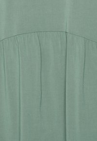 Tecido verde menta com um leve brilho, apresentando uma costura franzida na área da cintura e uma textura suave em todo o tecido.