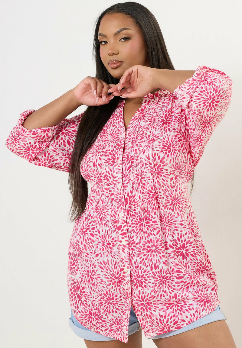 Camicia a maniche lunghe con un motivo floreale rosa su sfondo bianco, dal taglio rilassato e dotata di una chiusura frontale con bottoni.