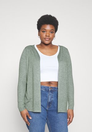 Lysegrøn cardigan med åbent foran, lange ærmer og en blød tekstur, båret over en hvid cropped top og blå højtaljede jeans.
