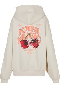 Krém színű kapucnis felső, amelyen két cseresznye grafikai nyomata látható, az "KANI MUSIC" felirat pedig élénk narancssárga betűkkel van kiemelve. Kenguruzsebes és bordás mandzsettákkal rendelkezik.