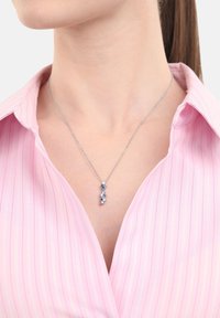 Silvrig kedja med en vertikal hänge av växelvis blå och vita ädelstenar som bärs av en person i en rosa randig skjorta.