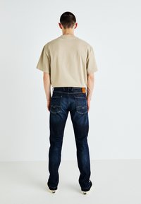 Beige puuvillane t-särk ja tume sinine denimist teksapüksid. Teksad sisaldavad nahkpleki ning kontrastne niit tagakottides.