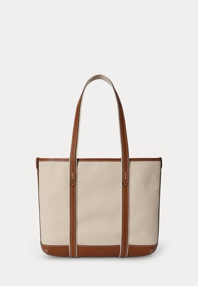 Sac cabas en toile beige avec poignées, garnitures et détails de base en cuir marron, présenté sur un fond clair uni.