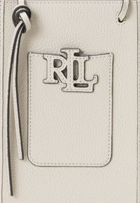 Kreemvärvi nahktool, millel on esiküljel reljeefne RL logo. Tekstureeritud pind, kontrastse tumeda õmblusega ja tõmbluku sulgemisega.
