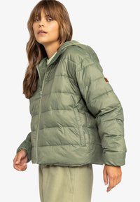 Grøn pufferjakke med hætte, quiltet design, frontlynlås og sidelommer. Tekstureret, vandafvisende materiale. Brun logoaccent.