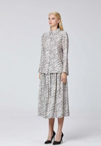 Ensemble comprenant une chemise boutonnée et une jupe en blanc avec des lignes ondulées noires. Texture soyeuse, manches longues, col montant et jupe fluide. Escarpins noirs.