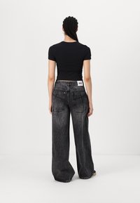 Černý přiléhavý top s krátkým rukávem ve spojení s vysokými širokými kalhotami v vybledlém černém denim. Obsahuje zadní kapsy a značkovou visačku.