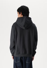 Sweatshirt à capuche gris foncé avec une finition texturée, doté d'une grande capuche, de poignets côtelés et d'une taille côtelée, associé à un pantalon en denim bleu.