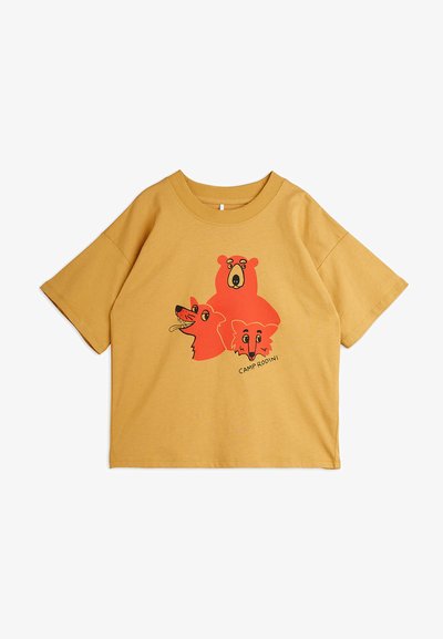 T-shirt de algodão amarelo com mangas curtas, apresentando uma ilustração de um urso, uma raposa e um cão em vermelho, com o texto "CAMP RODINI" abaixo.