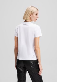 White short-sleeve t-shirt with a crew neck. Features a small "Karl Lagerfeld" label at the back and a simple graphic detail at the hem.