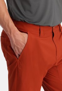 Rode stretch stof broek met een slanke pasvorm, voorzien van zijzakken, een ritssluiting en een subtiele merkdetail nabij de zak.