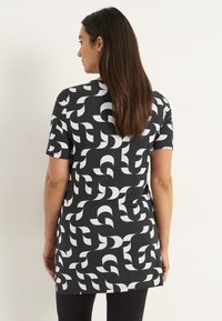 Zwart T-shirt met korte mouwen, versierd met een wit abstract patroon, gemaakt van een soepele stof. Het ontwerp bevat verschillende gebogen vormen.