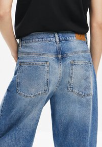 Ljust blå denimjeans med h�ög midja, med två bakfickor och en brun läderpatch i midjan. Tyget har en lätt blekt textur.