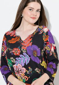 Schwarze Bluse mit bunten Blumenmustern in Lila, Orange und Grün, mit V-Ausschnitt und drei Viertelärmeln.