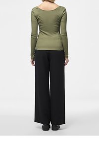 Olivově zelený žebrovaný top s dlouhým rukávem a vykrojeným zadním dílem, spárovaný s volnými černými kalhotami širokého střihu a černou obuví, pohled zezadu.