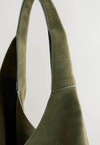 Olivengrøn ruskinds taske med glat tekstur, der har robuste håndtag og tonale syninger. Designet fremhæver enkelhed og funktionalitet.