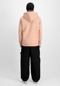 Felpa rosa polveroso con cappuccio regolabile, texture morbida e polsini a costine, abbinata a pantaloni cargo neri larghi con tasche laterali.
