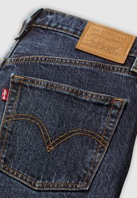 Mørkeblå denimjeans baglomme med orange syninger, Levis røde mærke og tanfarvet læderlogo fra Levi Strauss & Co.
