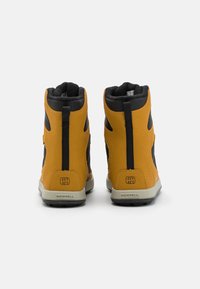 Bottes étanches jaunes avec accents noirs, en matériau synthétique texturé, design mi-hauteur et semelles en caoutchouc. Comprend le logo de la marque et des détails sur la plage de température.