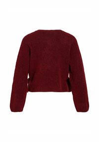 Bordo spalvos trumpas megztinis iš minkštos medžiagos, su ilgomis rankovėmis ir tiesia apačia. Šonuose yra plyšiai, užtikrinantys geresnį orui pralaidumą.