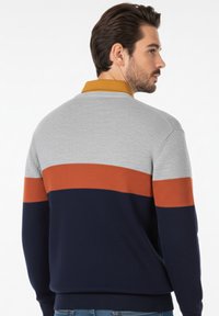 Suéter de punto en gris, azul marino y naranja con un cuello amarillo. Presenta bloques de color horizontales y un dobladillo acanalado. Ajuste casual, textura de peso medio.