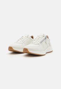 Weiße Leder-Sneaker mit einer strukturierten Gummisohle, Schnürdesign und seitlichem Reißverschlussdetail. Hellbraune Akzente in der Nähe der Ferse.