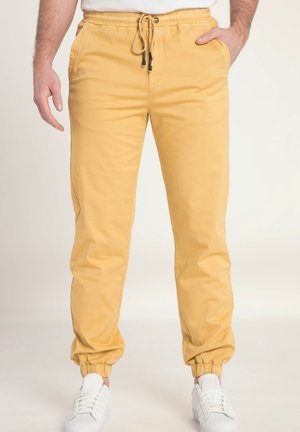 Pantalons de jogging en coton jaune avec une taille élastique et un cordon de serrage. Dotés de poches latérales et de poignets fuselés, associés à des baskets blanches.