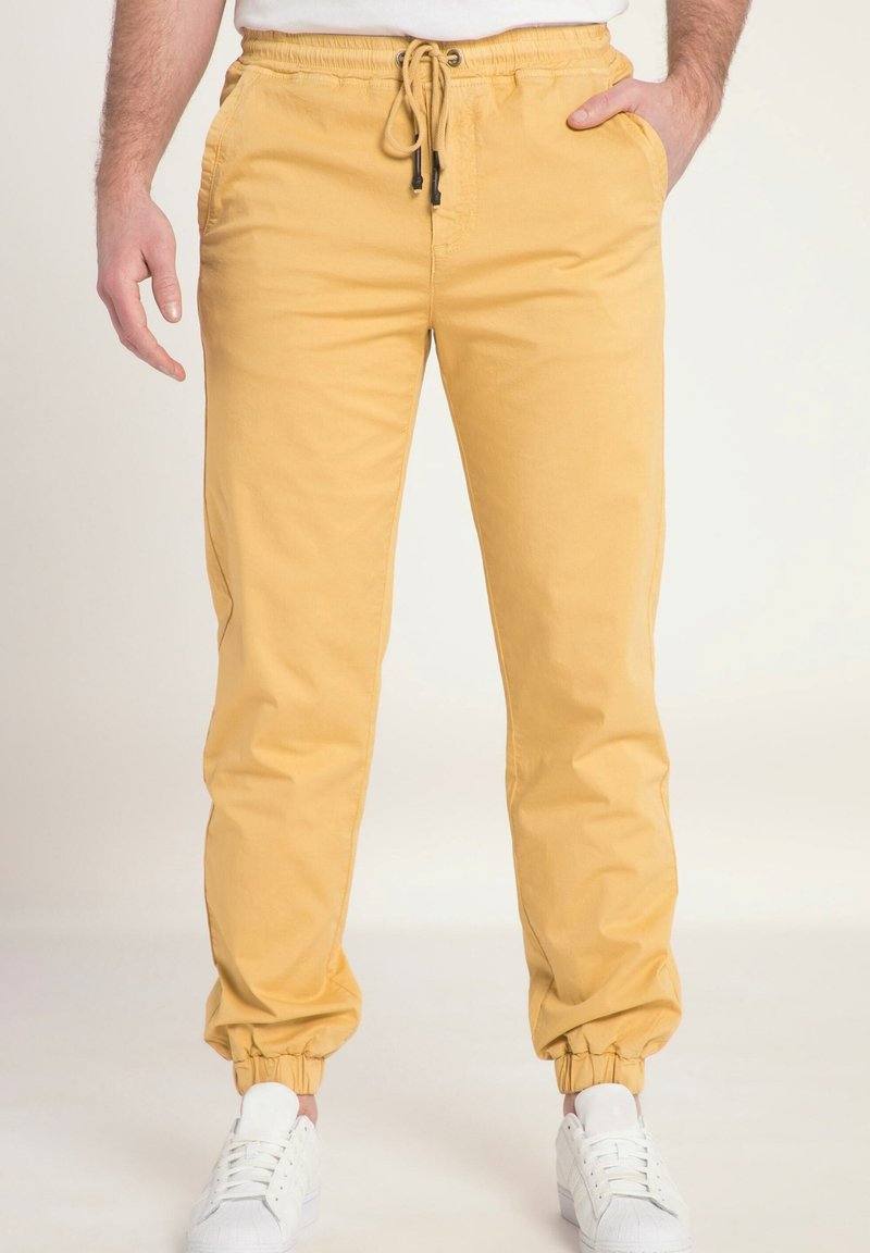 Gele katoenen joggerbroeken met een elastische tailleband en trekkoord. Voorzien van zijzakken en taps toelopende boorden, gecombineerd met witte sneakers.