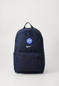 Tamsiai mėlyna kuprinė su apvalia viršutine dalimi, priekiniame dizaine su užtrauktuko kišene, Nike logotipu ir apskrita mėlynos ir baltos spalvos komandos emblema.