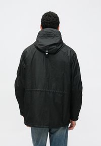 Schwarze Kapuzenjacke mit lässiger Passform, strukturiertem Stoff und verstellbaren Kordeln an Kapuze und Taille. Minimalistisches Design.