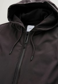 Mustmust suursärk musta värvi, millel on sile, mati viimistlus, varustatud reguleeritava kapuutsi ja diskreetse brändi sildiga krae sees.