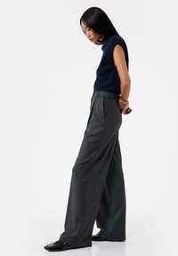 Marineblauwe mouwloze top gecombineerd met hoog-waist, brede grijze geruite broek. De outfit heeft strakke lijnen en een op maat gemaakte pasvorm.