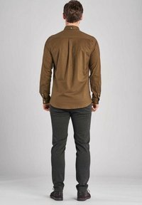 Brown button-up shirt with a back pleat, paired with dark gray trousers. Fabric appears smooth; shirt features long sleeves and buttons at cuffs.