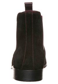 Musta mokkangommon nilkkuri, jossa on sileä pinta, minimalistinen muotoilu, joustavat sivupaneelit ja eroava punainen tikkaus takaosassa.