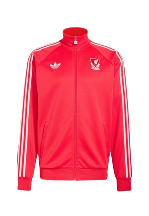 Punainen vetoketjullinen urheilutakki, jossa valkoiset Adidas-raidat hihassa, Adidas-logo oikeassa rinnassa ja Liverpool FC:n tunnus vasemmassa rinnassa.
