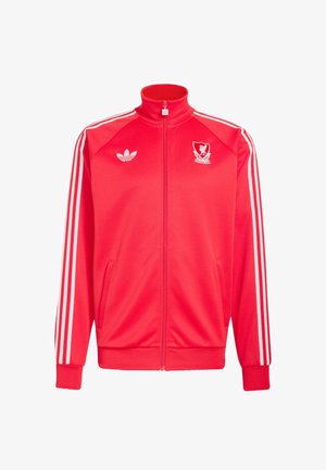 Punainen vetoketjullinen urheilutakki, jossa valkoiset Adidas-raidat hihassa, Adidas-logo oikeassa rinnassa ja Liverpool FC:n tunnus vasemmassa rinnassa.