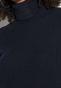 Merinovihreä resorineuleinen t-paita, jossa on istuva muotoilu. Kankaassa on pystysuoria viivoja ja korkea kaulus, joka takaa mukavan istuvuuden.