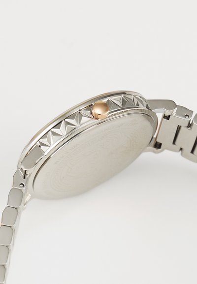 Roostevaba terasest kell läikiva hõbedase korpuse, tekstuurse pöörleja, millel on püramiidikujulised detailid, ja kuldse krooniga. Rihm koosneb rectangulaarsetest linkidest.