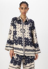Camicia a maniche lunghe con bottoni in crema e blu navy, presenta un motivo paisley con dettagli intricati. Tessuto morbido, vestibilità rilassata.