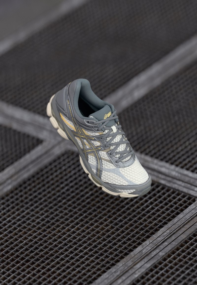 Gray and white running shoe with mesh upper, textured detailing, and yellow accents; features a cushioned sole and sturdy laces.