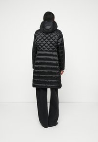 Casaco puffer preto com padrões de diamante e acolchoados horizontais, apresentando capuz e corte a meio da coxa. O tecido tem uma textura brilhante e suave.