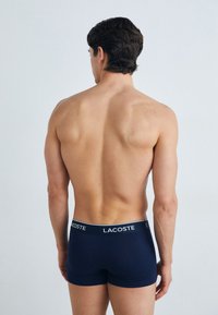 Boxers en bleu marine avec une coupe ajustée, arborant un logo Lacoste blanc sur la ceinture. Tissu lisse, design minimaliste.