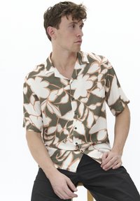 Short-sleeve shirt featuring a beige and olive floral pattern, with black buttons and a camp collar. The fabric appears lightweight and smooth.