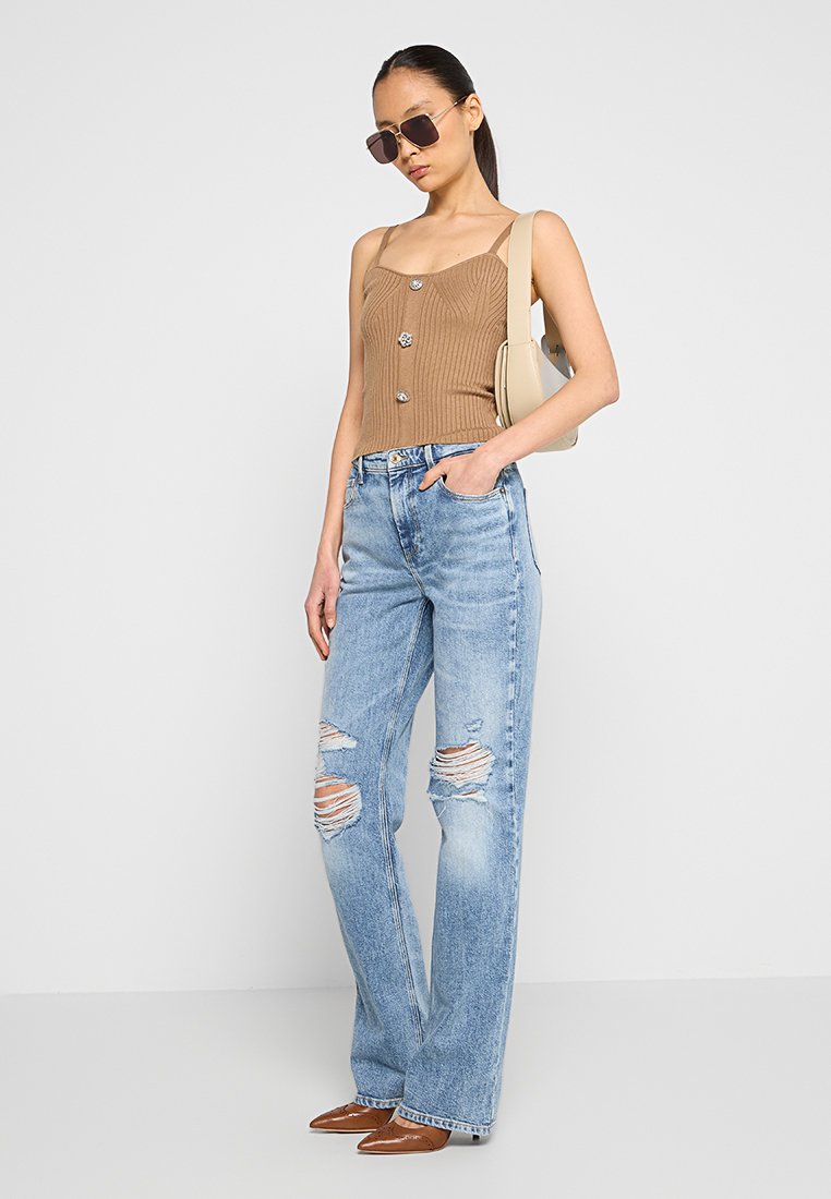 Braunes, geripptes Tanktop mit Knopfdetails, kombiniert mit hellblauen, ausgewaschenen, weiten Jeans und braunen Spitzenschuhen. Die Accessoires umfassen Sonnenbrillen und eine beige Handtasche.